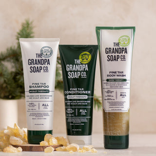 The Pine Tar Bundle Body Wash and Haircare Bundle stands upright on a surface, with pine branches and resin pieces in the background.